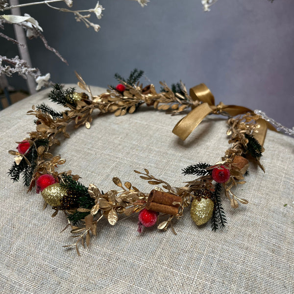 Golden Christmas flower wreath with cinnamon sticks and evergreen branches and with a ribbon at the back to tie